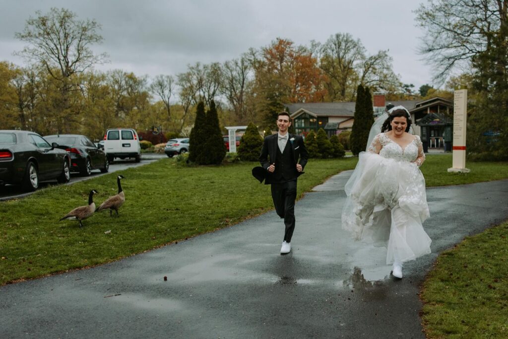 Bride and groom running together laughing on rain-soaked path at Elizabeth Park West Hartfor