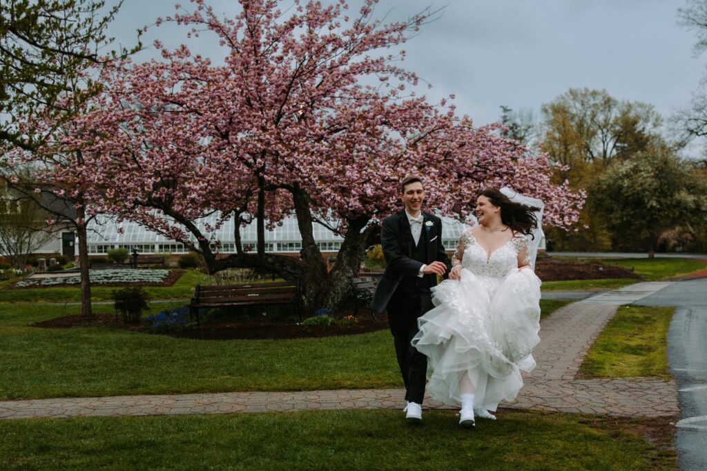 Couple walking and laughing through Elizabeth Park with cherry blossoms, Pond House wedding
