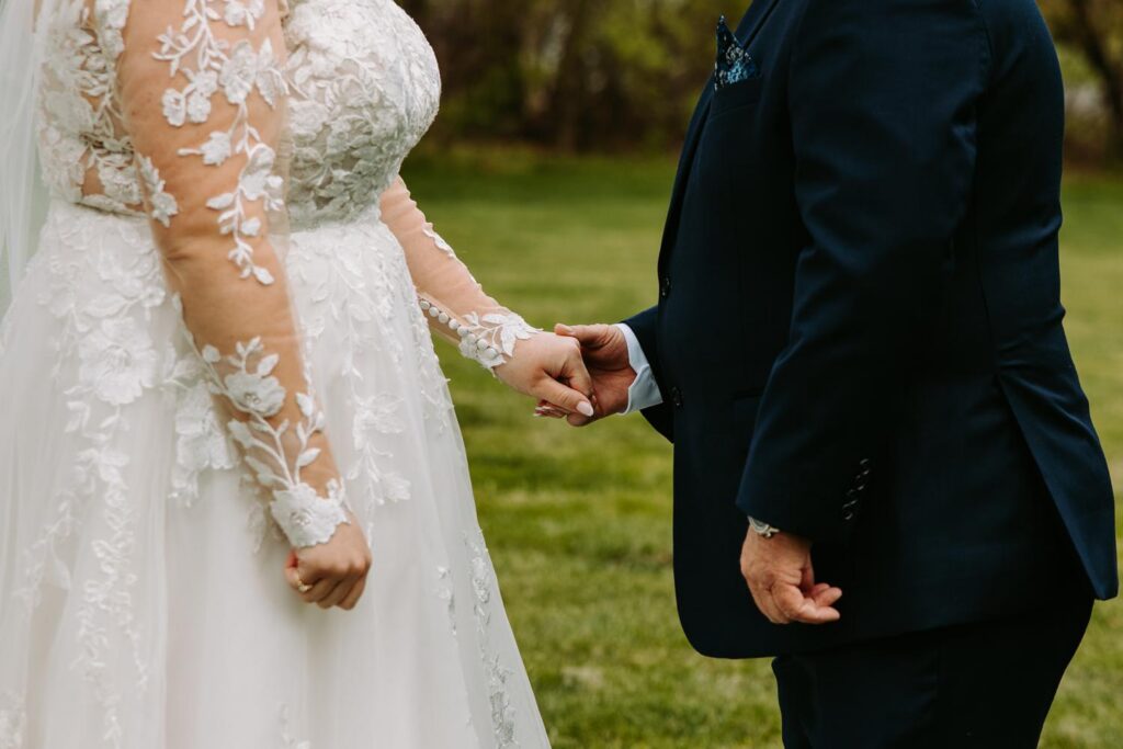 Close-up detail of bride and grandfather holding hands, lace sleeve and suit cuff