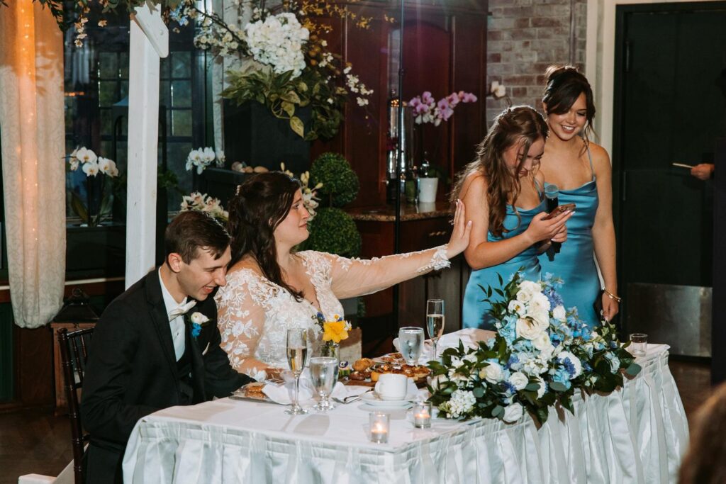 Bride laughing with sisters during toast at reception table, Pond House wedding