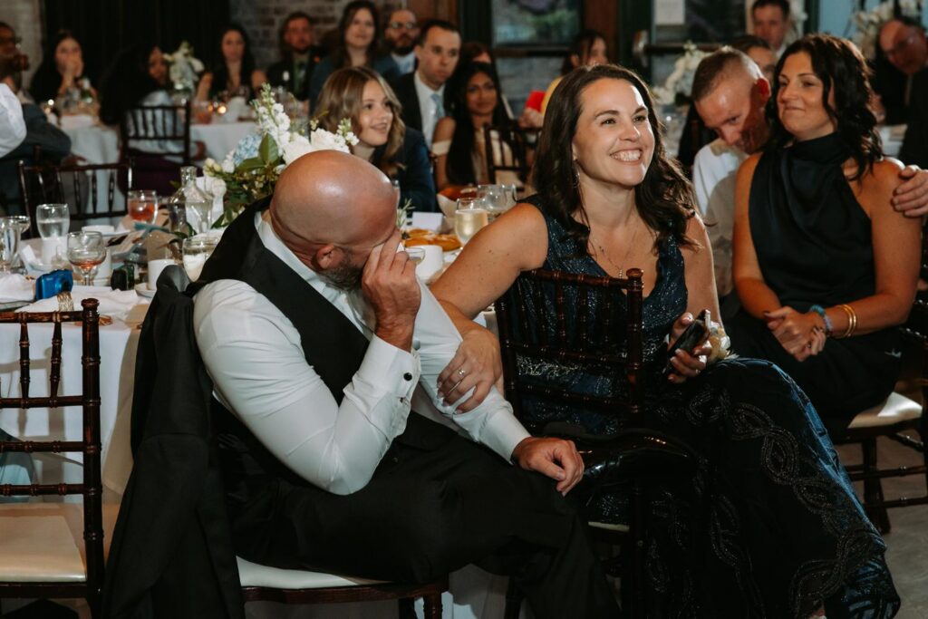 Family seated at reception table laughing together, candid documentary wedding moment