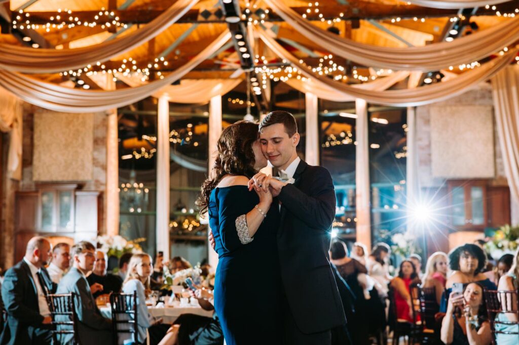 Groom and mom under draped ceiling with string lights, Pond House Cafe reception room