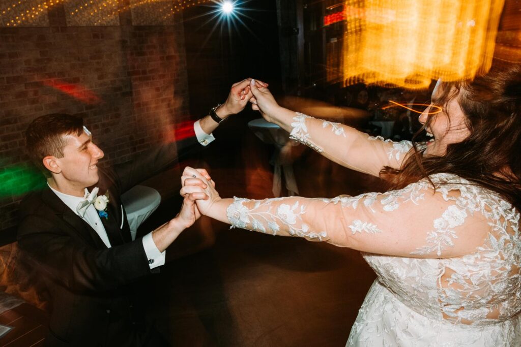 Bride and groom dancing energetically together on the dance floor, lace wedding dress in motio