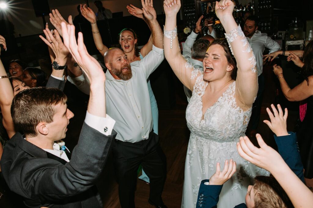 Guests with hands raised celebrating on the dance floor, high energy wedding reception