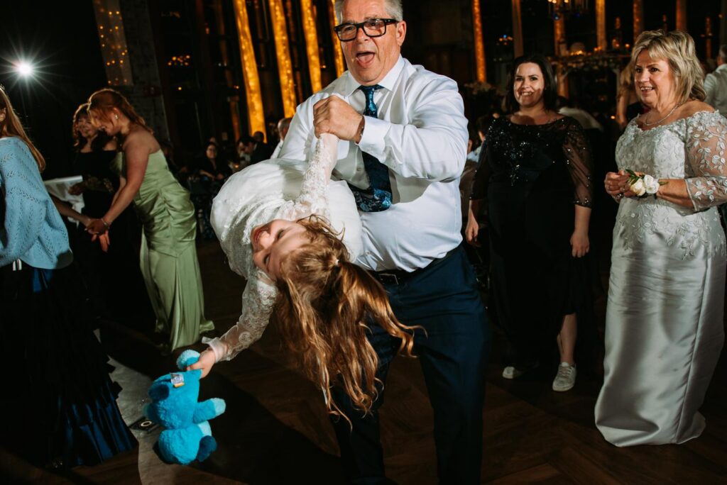 Grandfather dipping flower girl on the wedding dance floor, joyful family moment