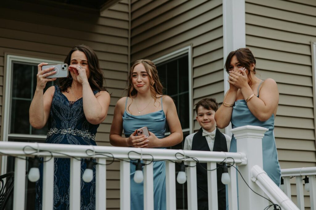 Bridesmaids and reacting with tears and laughter watching from a deck during first look