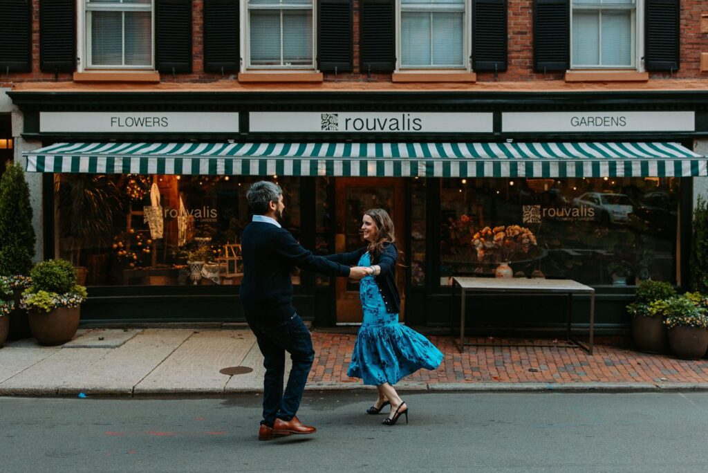 Couple dancing and laughing together in front of Rouvalis Flowers and Gardens on Charles Street Beacon Hill, blue dress twirling