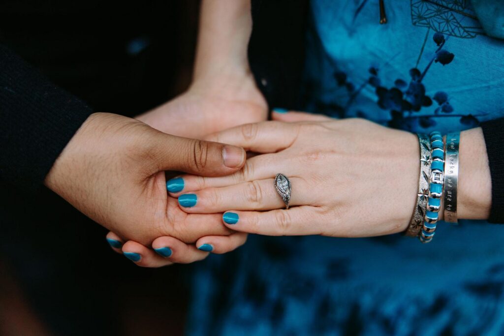 Close up of Kelsey and Ankit's hands intertwined showing engagement ring and blue nail polish against the blue floral grandmother's dress
