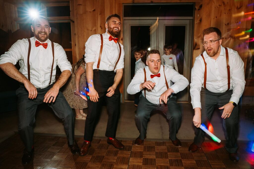 Groomsmen in matching suspenders and red bow ties doing a synchronized group dance move, Bluebird Farm reception