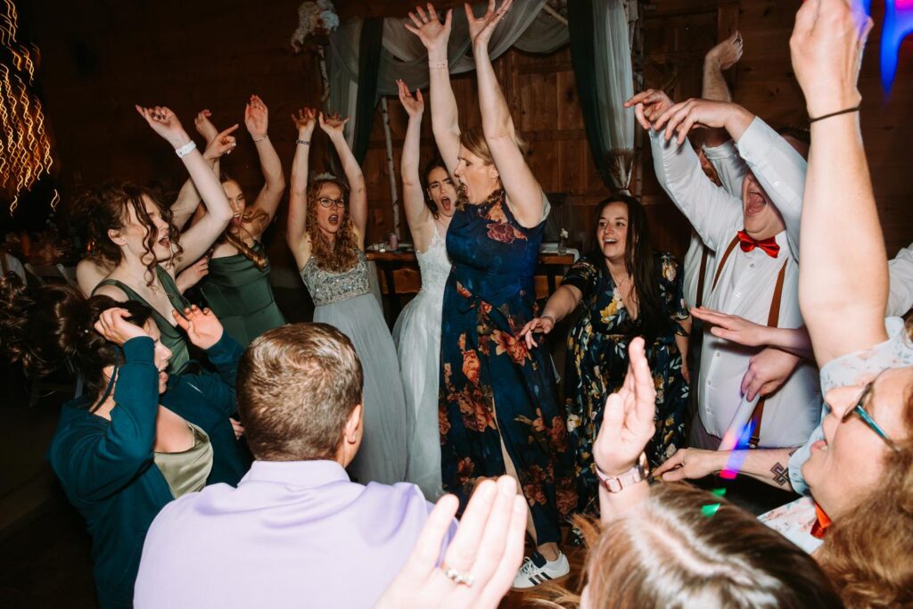 Dance floor chaos at its peak, everyone jumping with hands raised, late night Bluebird Farm wedding