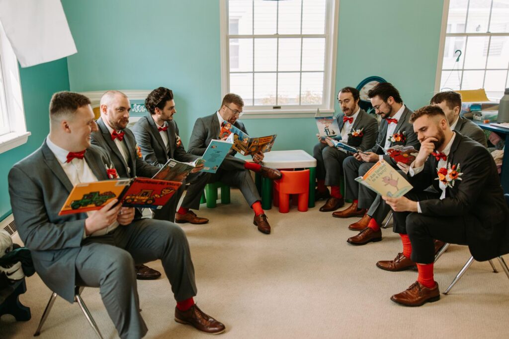 Groomsmen sitting in a circle reading children's books as a getting ready activity, groom's red socks visible, Bluebird Farm wedding