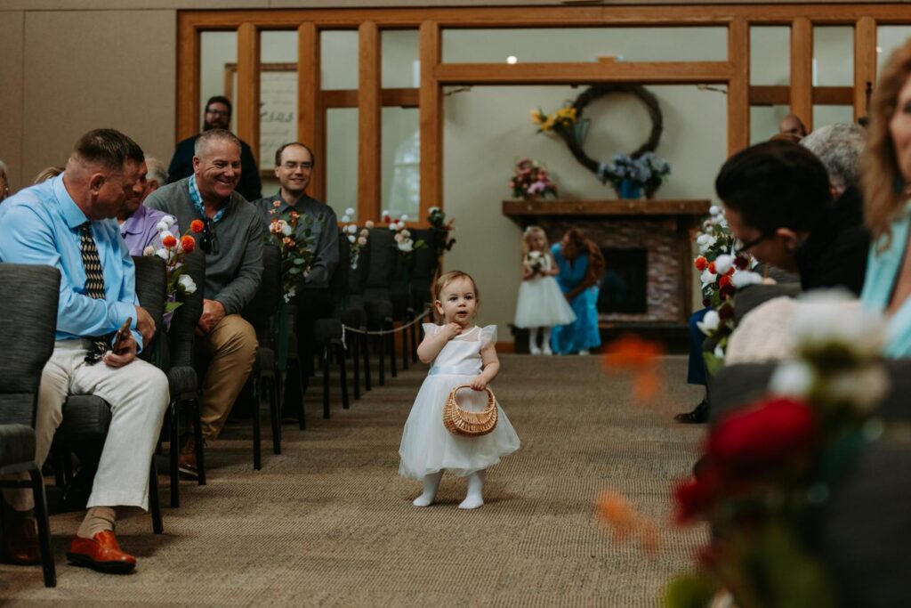 Flower girl tossing petals while walking down the aisle, guests watching from their seats, church ceremony at Bluebird Farm wedding