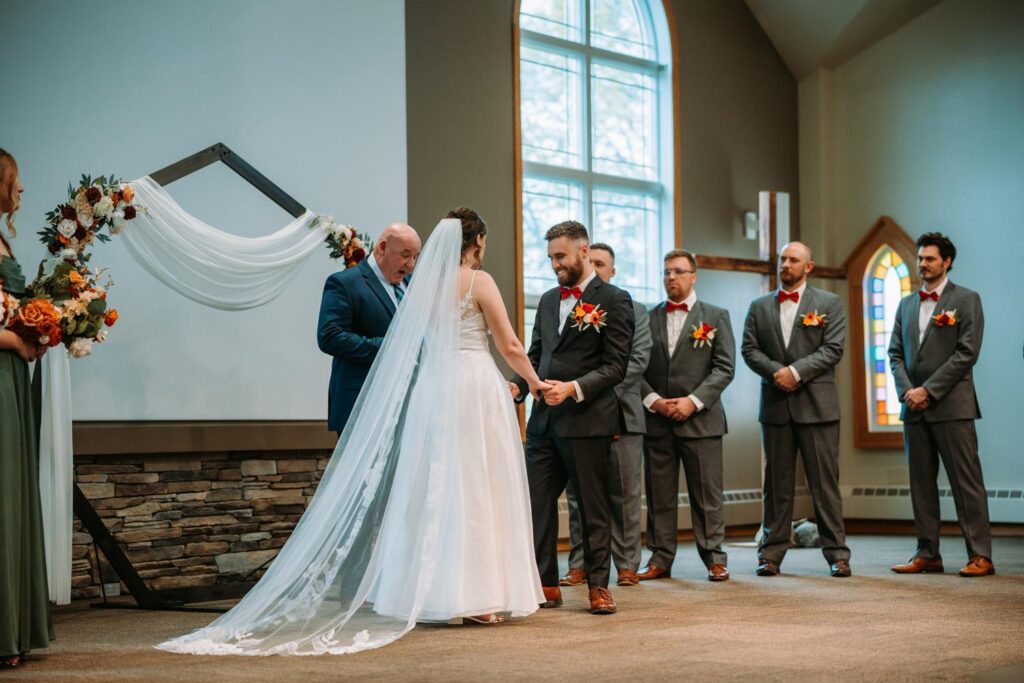 Wide shot of wedding ceremony with bride and groom at altar, floral wooden arch, and full seated guest attendance