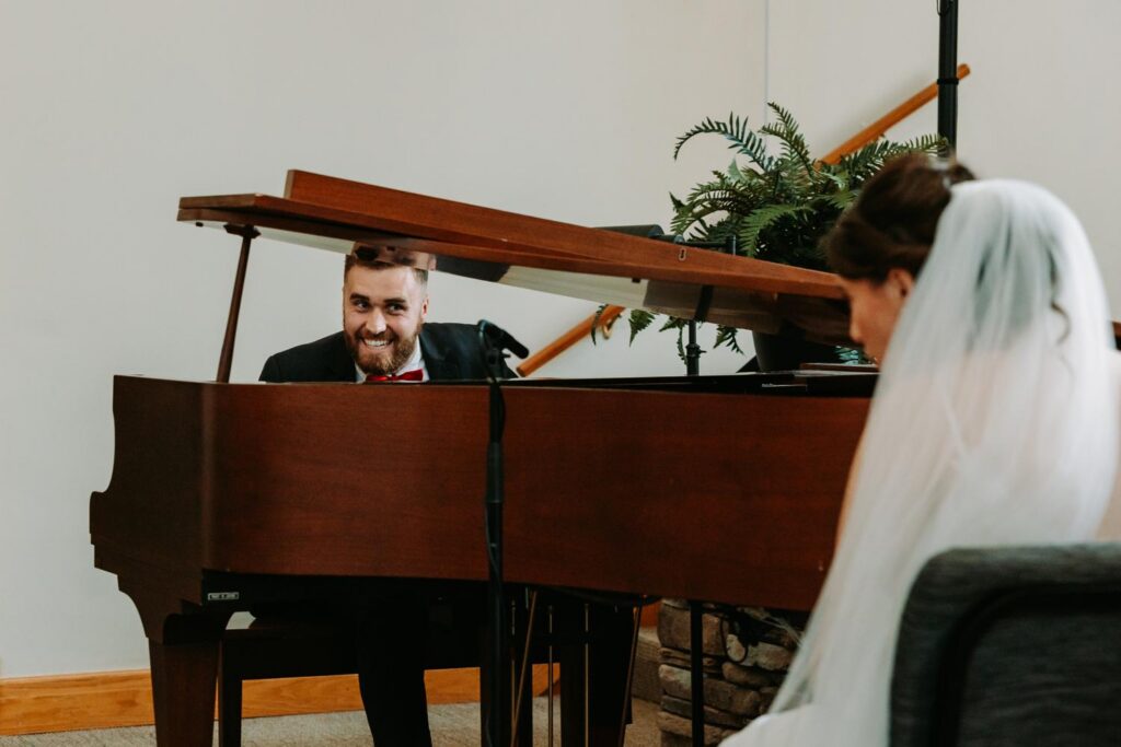 Groom looking up from the piano smiling at his bride during his surprise piano performance, Bluebird Farm wedding