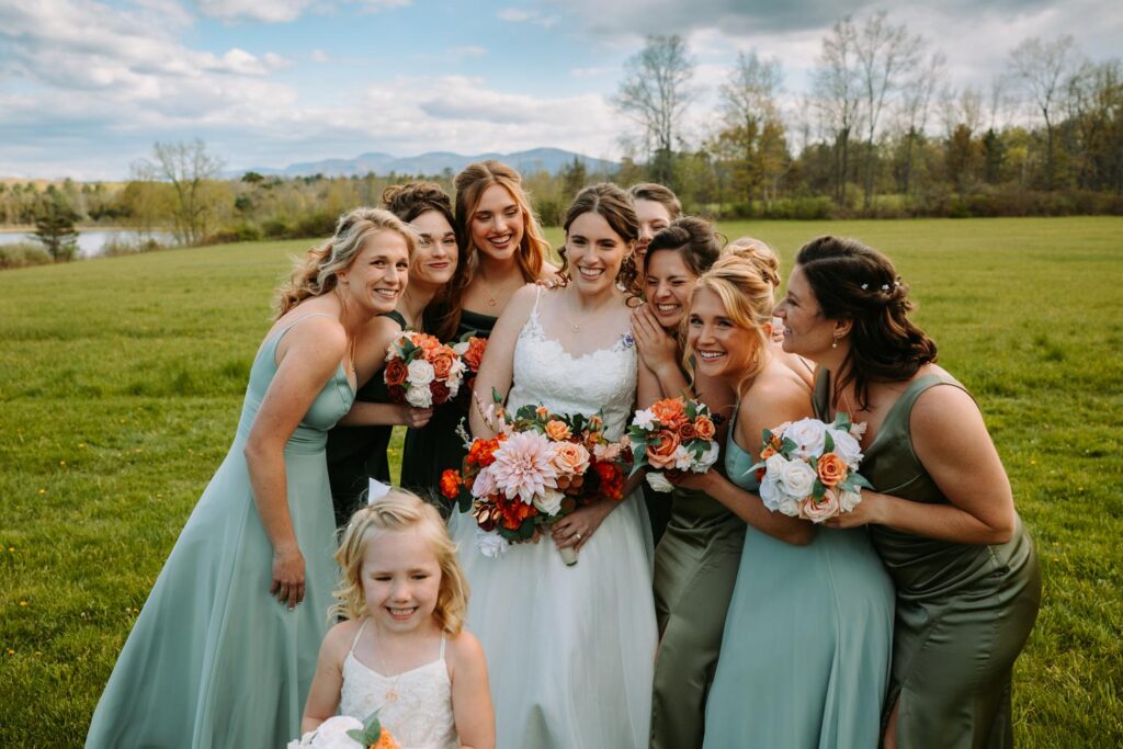 Bridesmaids in sage green dresses with bride in the open Bluebird Farm field, mountain view behind them