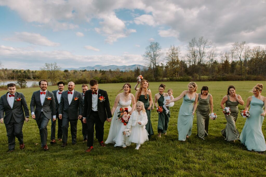 Full wedding party walking across the open field at Bluebird Farm with the Catskill Mountains as a backdrop, wide landscape shot