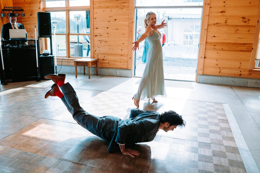 Groomsman doing the worm on the barn dance floor in his Red Sox socks, guests cheering, Bluebird Farm reception