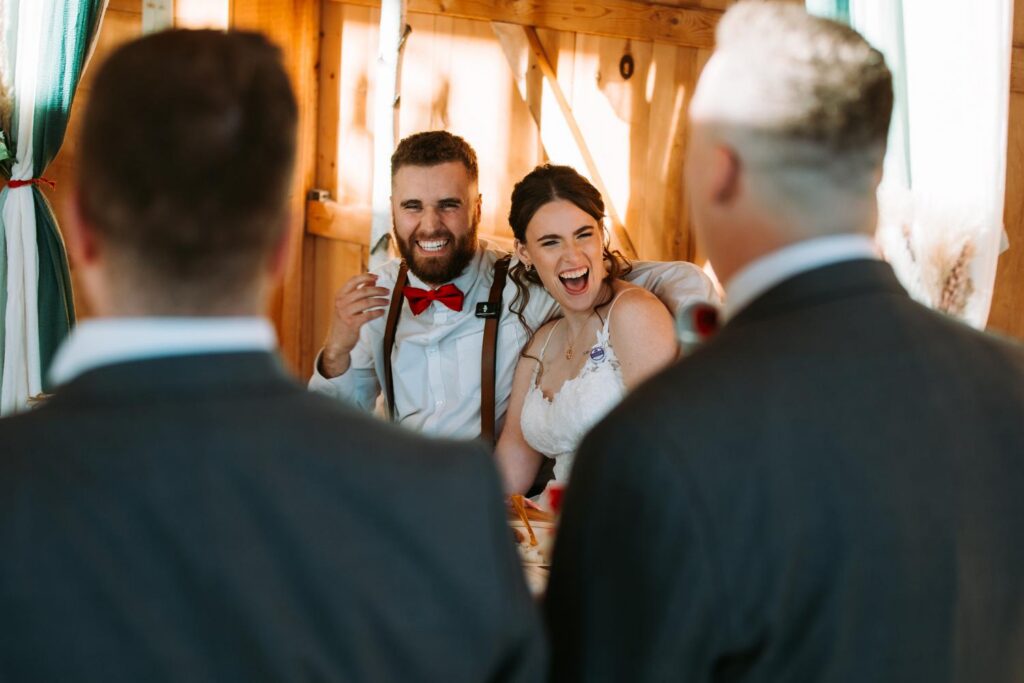Groom and bride laughing during a wedding toast inside the Bluebird Farm barn reception