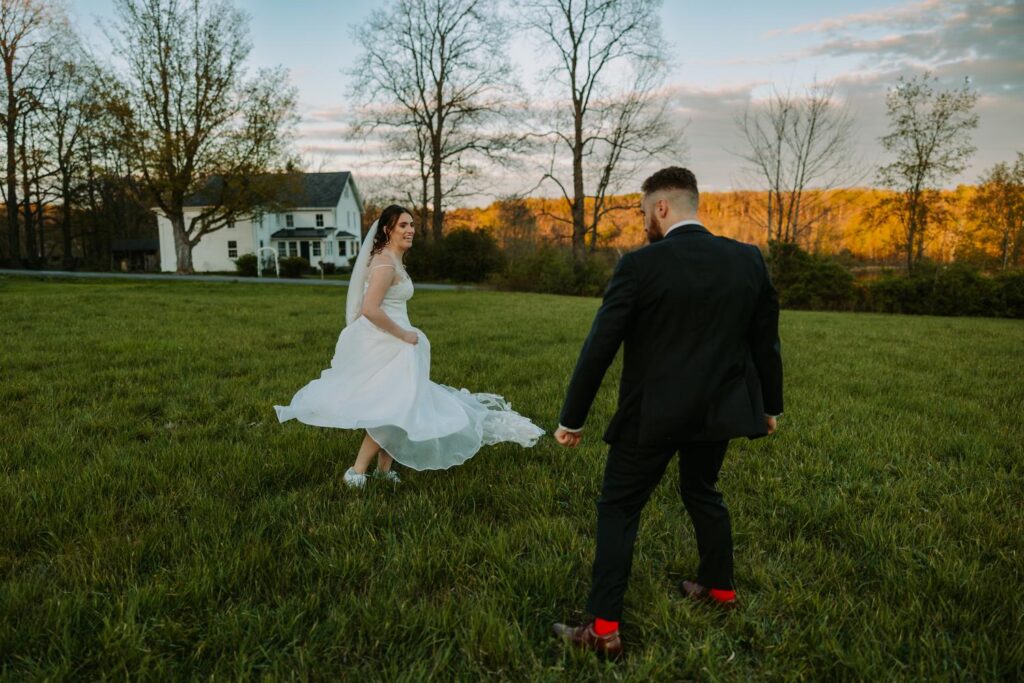 Bride dancing in the wide open field at Bluebird Farm, Catskill Mountains and glowing sky behind them