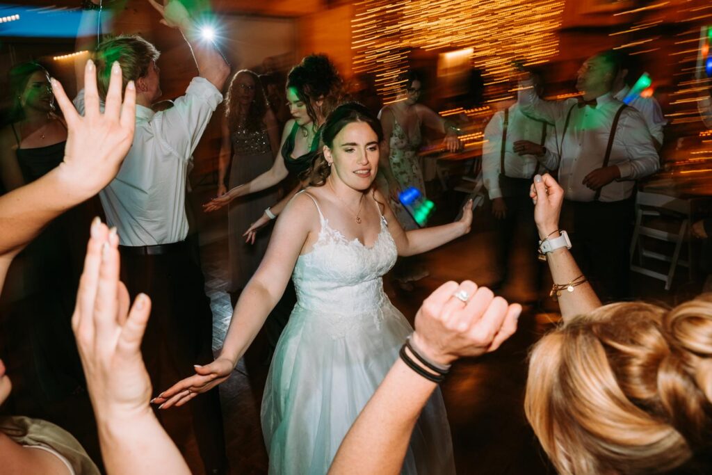 High energy full dance floor at Bluebird Farm, hands raised and motion blur, late night reception