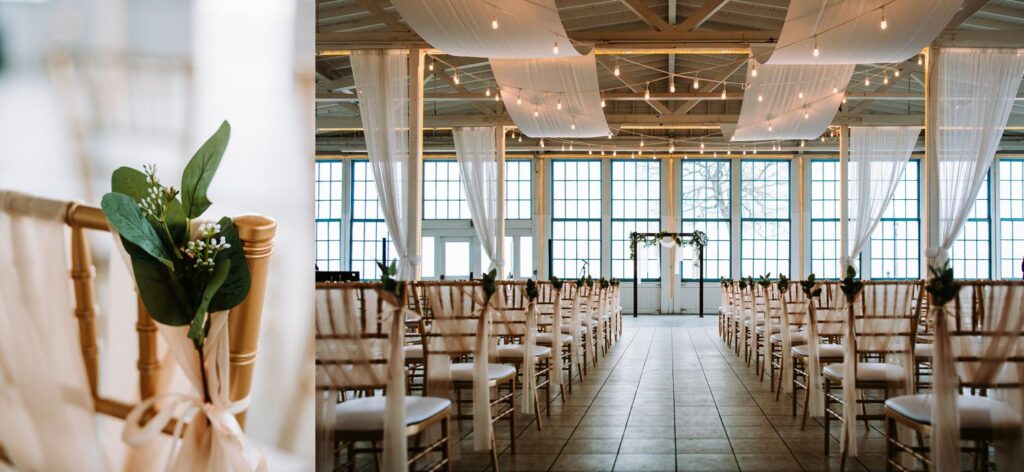Indoor ceremony setup at Lighthouse Point Park with white chiavari chairs, string lights, greenery floral arch, and large industrial windows