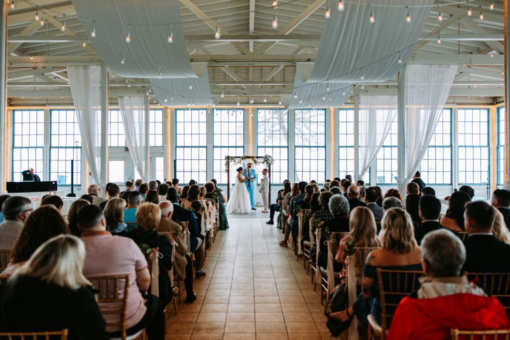 Wide aisle shot from the back of the ceremony space at Lighthouse Point Park, bride and groom tiny at the altar under the floral arch