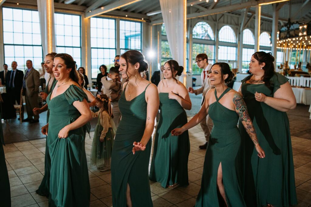 Bridesmaids in dark teal dresses dancing and making their grand entrance into the Lighthouse Point Park reception