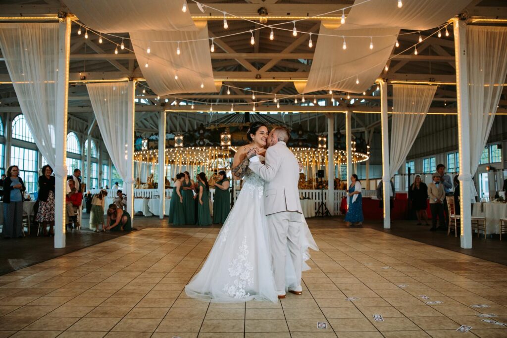 Wide shot of the first dance at Lighthouse Point Park, carousel lit up in the background, string lights above