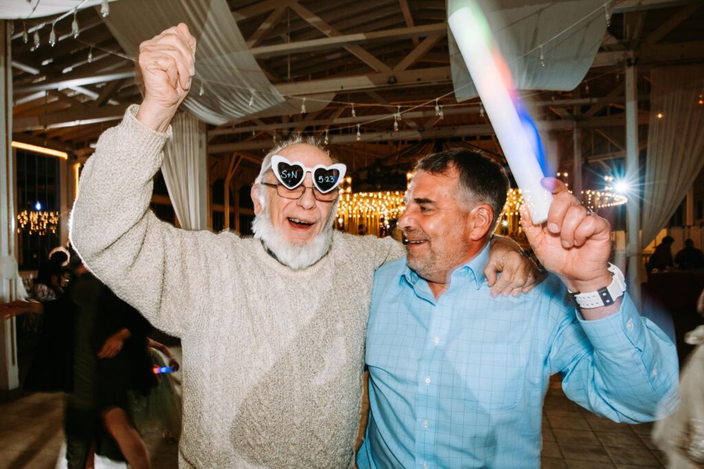 Older guest  dancing together with glow sticks, wide Lighthouse Point Park reception space glowing behind them